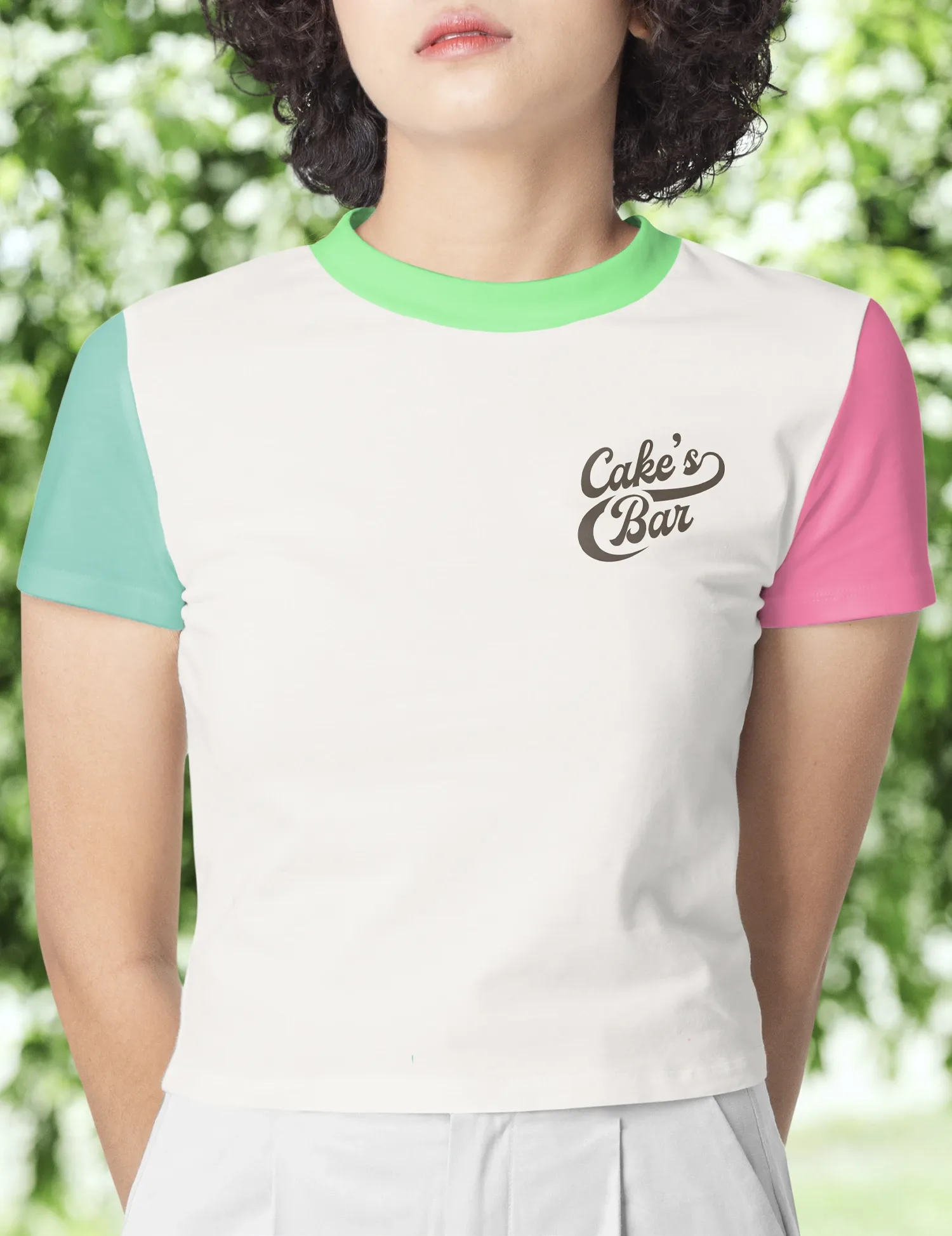 Una mujer muestra el uniforme de Cake's Bar. Una remera blanca, con una manga rosa y otra verde. Y sobre el pecho, a la altura del corazón, el logo de la marca en color chocolate.